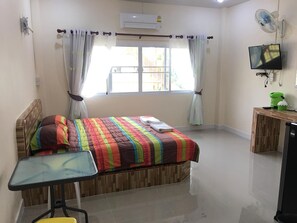 Un dormitorio con cama, una mesita, un televisor y una ventana con cortinas.