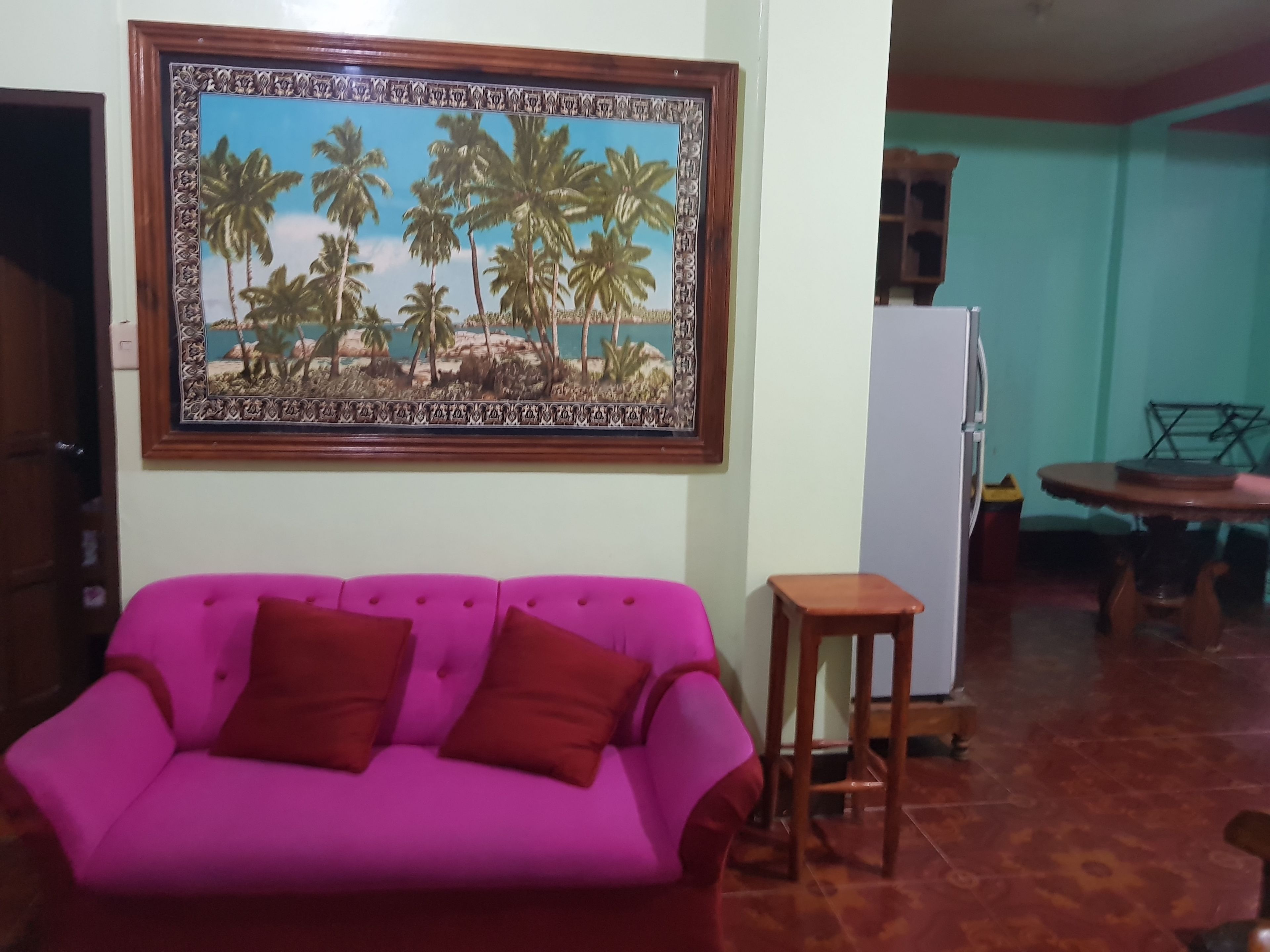A living room with a pink sofa, a wooden coffee table, and a painting of palm trees on the wall.