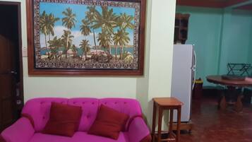 A living room with a pink sofa, a wooden coffee table, and a painting of palm trees on the wall.