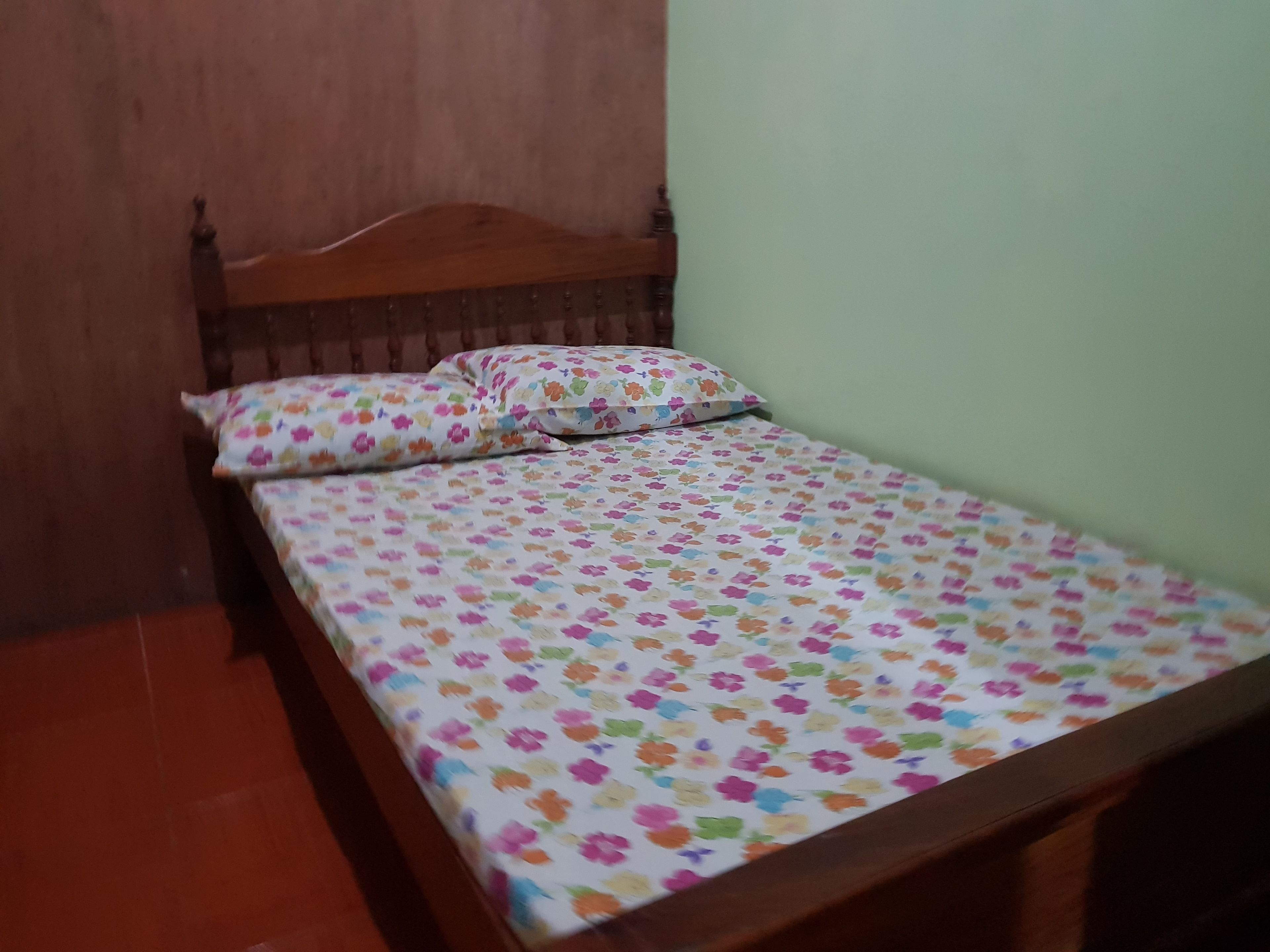 Ein kleines Zimmer mit einem Einzelbett, einem Holzkopfstück und einer zudecke mit Blumenmuster.