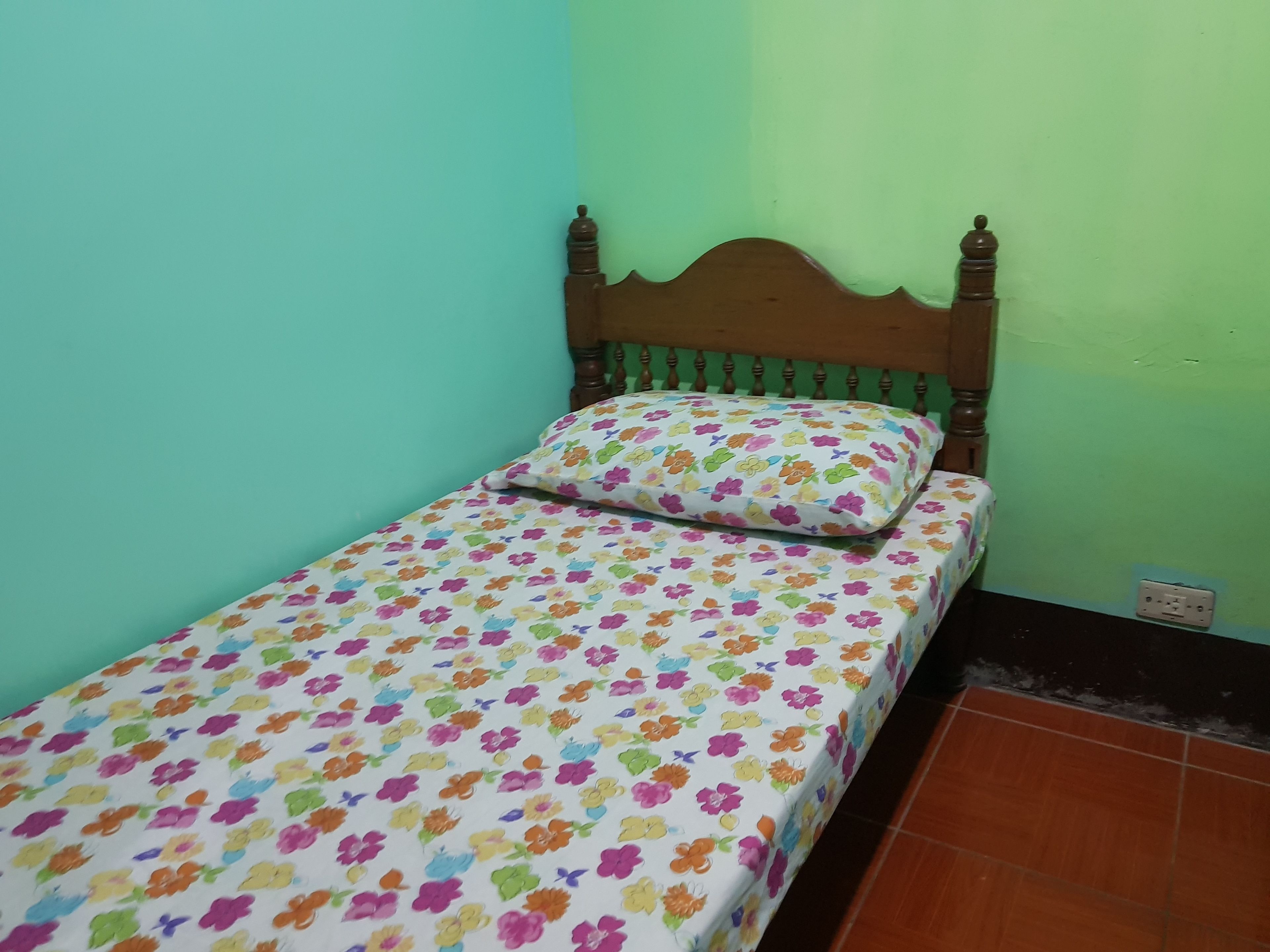 Una habitación pequeña con cama individual, cabecera de madera, colcha floral y pared verde.
