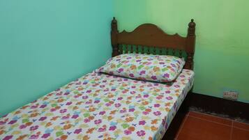 Una habitación pequeña con cama individual, cabecera de madera, colcha floral y pared verde.