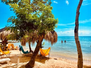 A beach with clear blue water, a thatched-roof hut, and several colorful beach chairs.