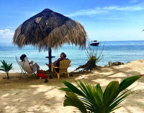 A beach scene with a thatched umbrella, two chairs, and a small table.