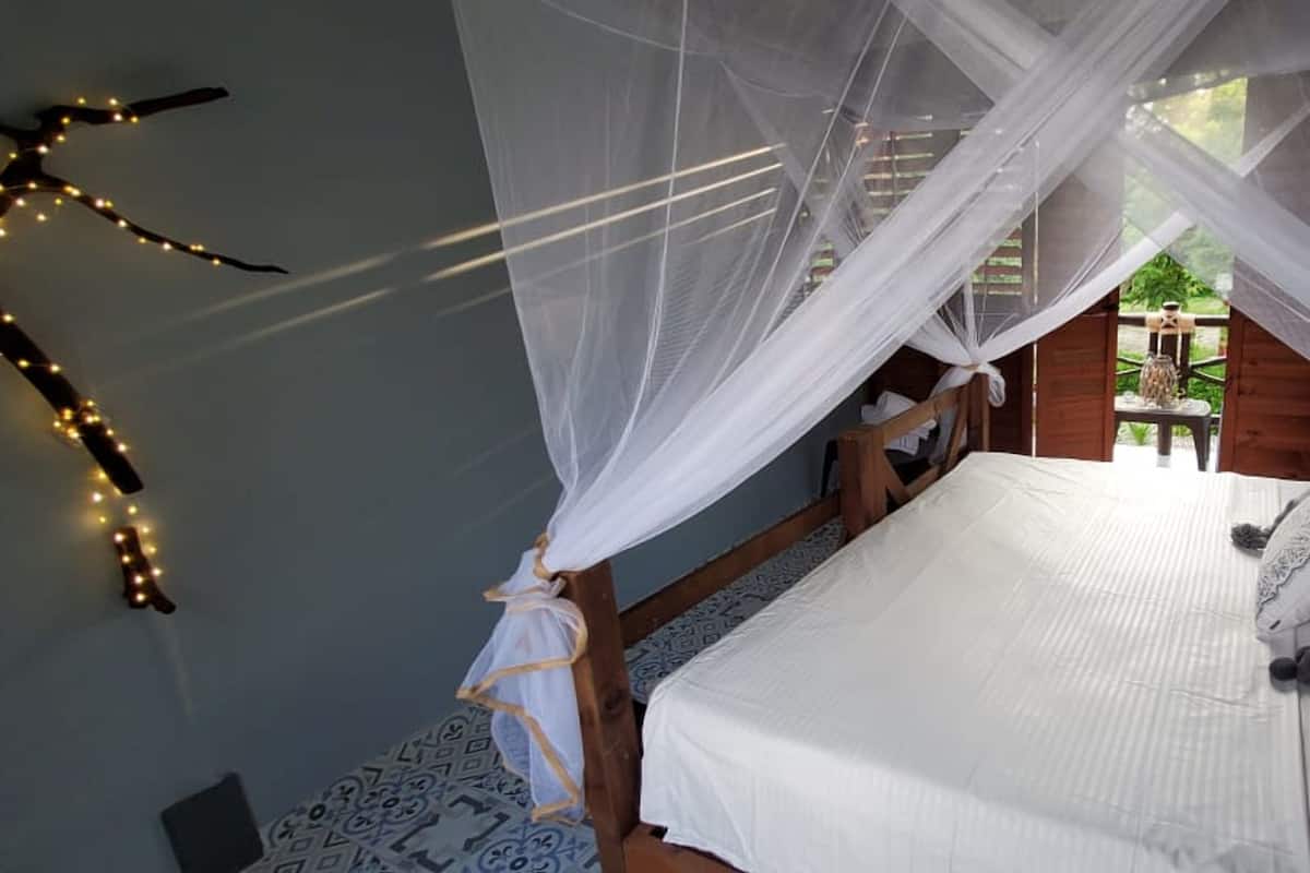Une chambre à coucher avec un lit, du linge de lit blanc, un baldaquin et une guirlande lumineuse décorative.