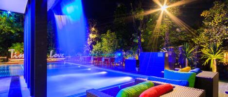 Un espace extérieur avec piscine, agrémenté d’un élément décoratif aquatique, de sièges et d’un éclairage décoratif.