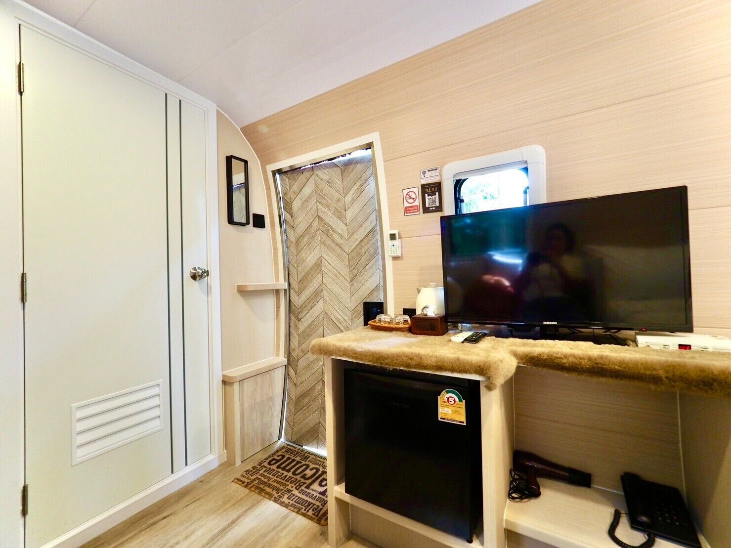 A hotel room with a television, a minibar, a phone, and a door.