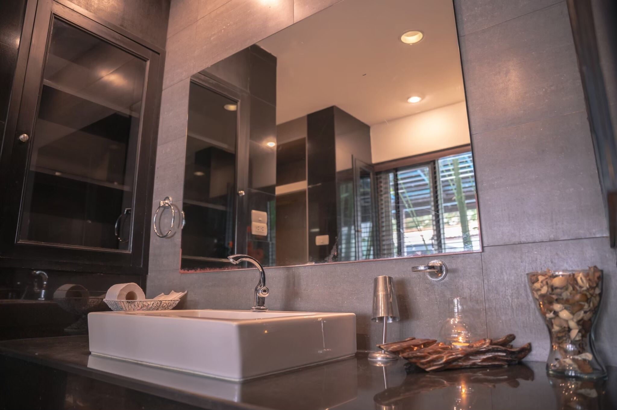 Une salle de bain moderne avec un grand miroir, un lavabo blanc et un vase décoratif.