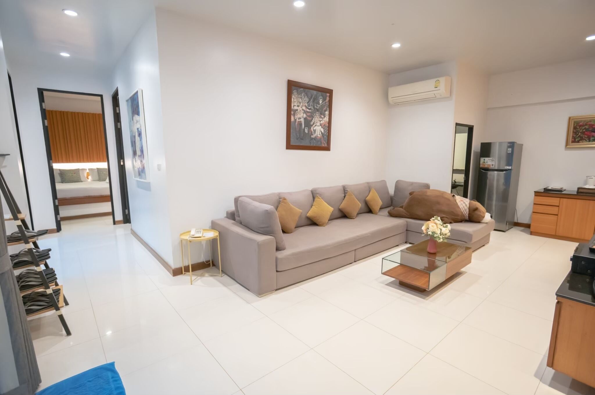 A modern living room with a grey sofa, a small side table, a coffee table, and a kitchen area with a refrigerator.