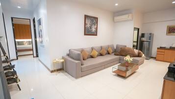 A modern living room with a grey sofa, a small side table, a coffee table, and a kitchen area with a refrigerator.