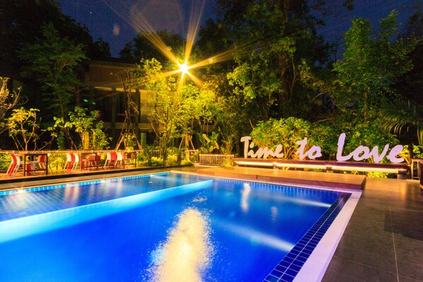 Piscina com um letreiro que diz 'Time to Love', rodeada por vegetação.