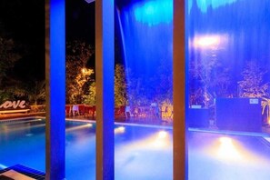Vista noturna de uma piscina com fontes iluminadas e um letreiro 'LOVE'.