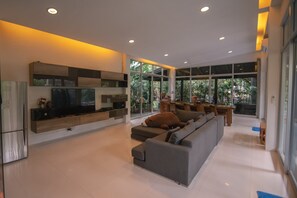 Uma sala de estar moderna com uma televisão de tela plana grande, um sofá cinza e um espaço de refeições com mesa e cadeiras.