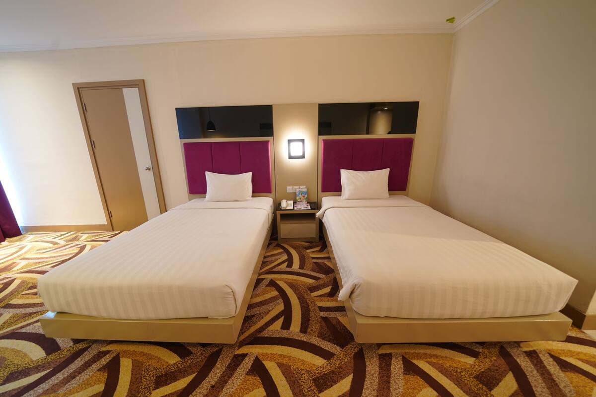 A hotel room with two beds, a nightstand, a mirror, and a patterned carpet.
