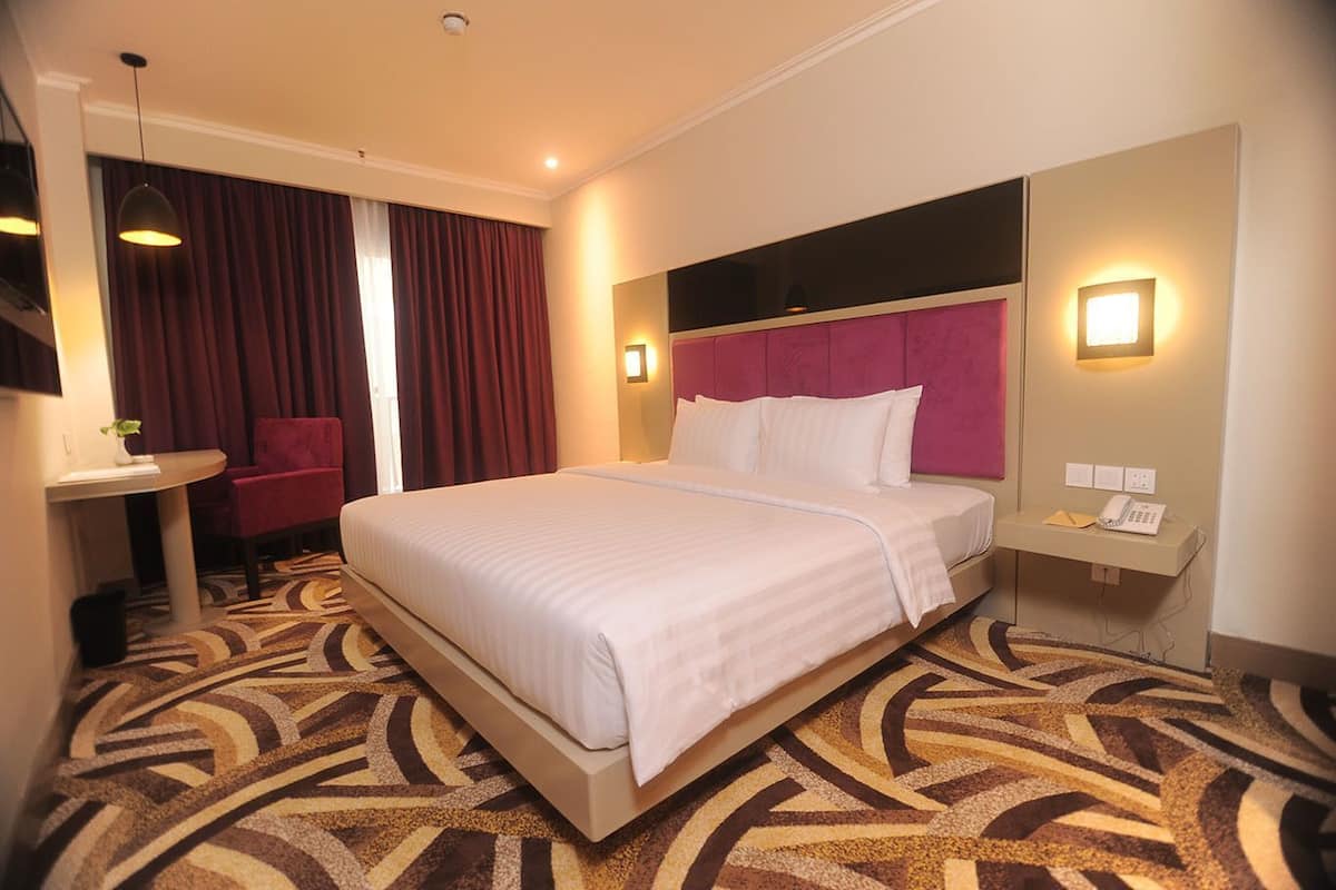 A hotel room with a bed, a desk, a chair, a mirror, and a telephone.