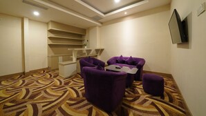 A hotel room with a patterned carpet, purple armchairs, a small table, a flat-screen TV mounted on the wall, and a staircase. - Ayola Sentosa Palembang (Palembang)