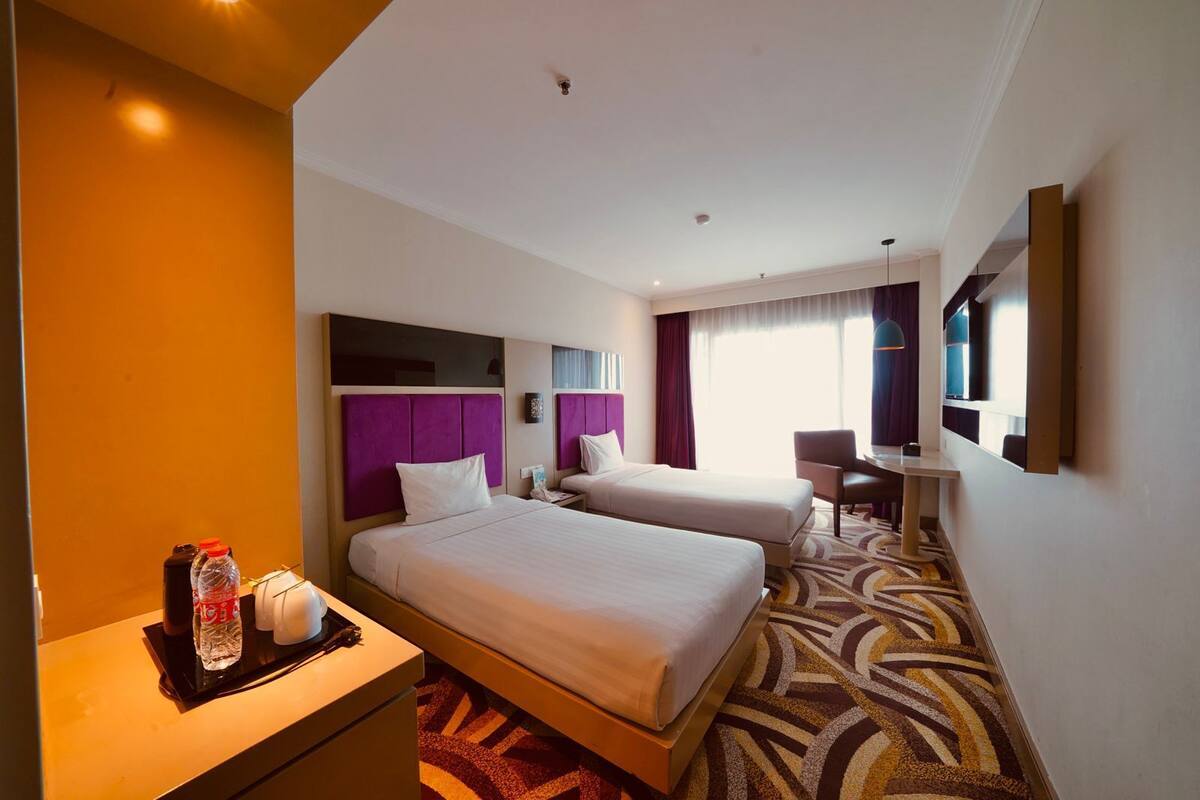 A hotel room with two beds, a desk, a chair, a TV, and a minibar.