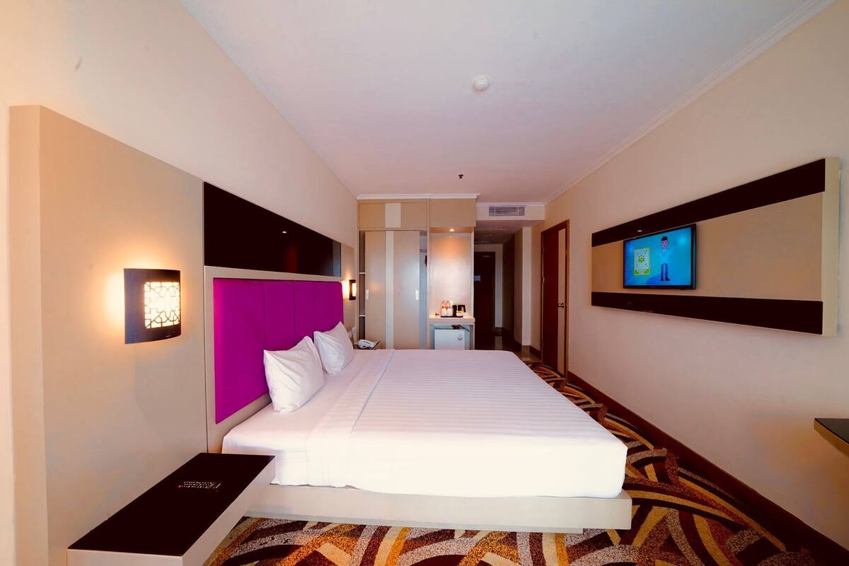 A hotel room with a large bed, a TV, a desk, and a bathroom visible through an open door.
