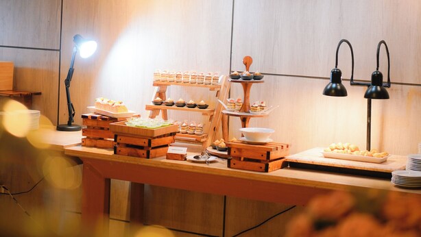A modern kitchen with wooden cabinets, pendant lights, and a buffet setup with various food items. - Ayola Sentosa Palembang (Palembang)