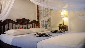 A bed with a canopy, a bedside table with a lamp, and a wall with newspaper wallpaper. - Banja Little Villa (Hikkaduwa)