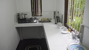 A compact kitchen with a gas stove, sink, and a window with vertical blinds. - Banja Little Villa (Hikkaduwa)
