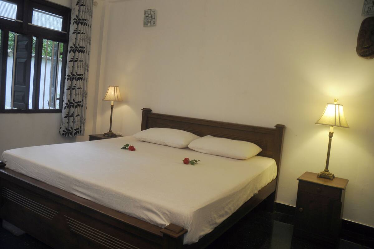 A neatly made bed with white linens, two bedside lamps, and a window with curtains.
