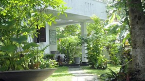 A garden pathway leading to a covered area with a bench and a table, surrounded by lush greenery and a white building. - Banja Little Villa (Hikkaduwa)