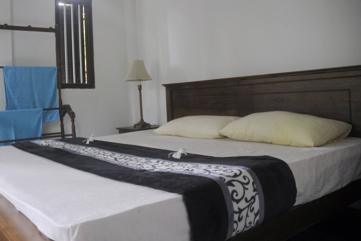 A bed with a wooden headboard, white bedding, and a black and white patterned throw.