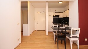 A compact kitchen with white cabinets, a black countertop, and a dining area with a table and chairs. - DRUSCHBA Boutique Apartment (Leipzig)