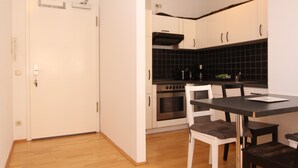 A modern kitchen with white cabinets, a black backsplash, and a wooden dining table with chairs. - DRUSCHBA Boutique Apartment (Leipzig)