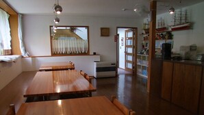 Un área de comedor con mesas y sillas de madera, una ventana con cortinas, un reloj y una puerta que da a otra habitación.