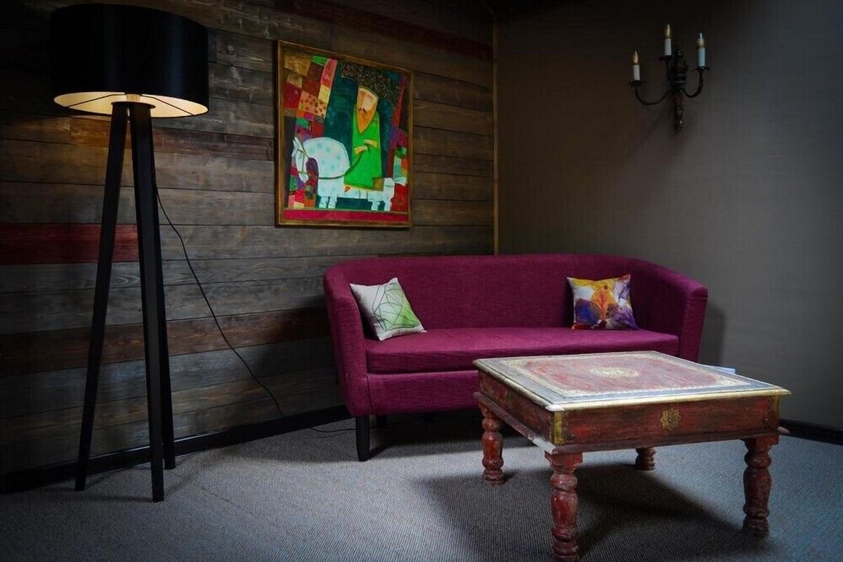 Una habitación con pared de madera, un sofá rojo, una mesita, una lámpara de pie y un cuadro llamativo.