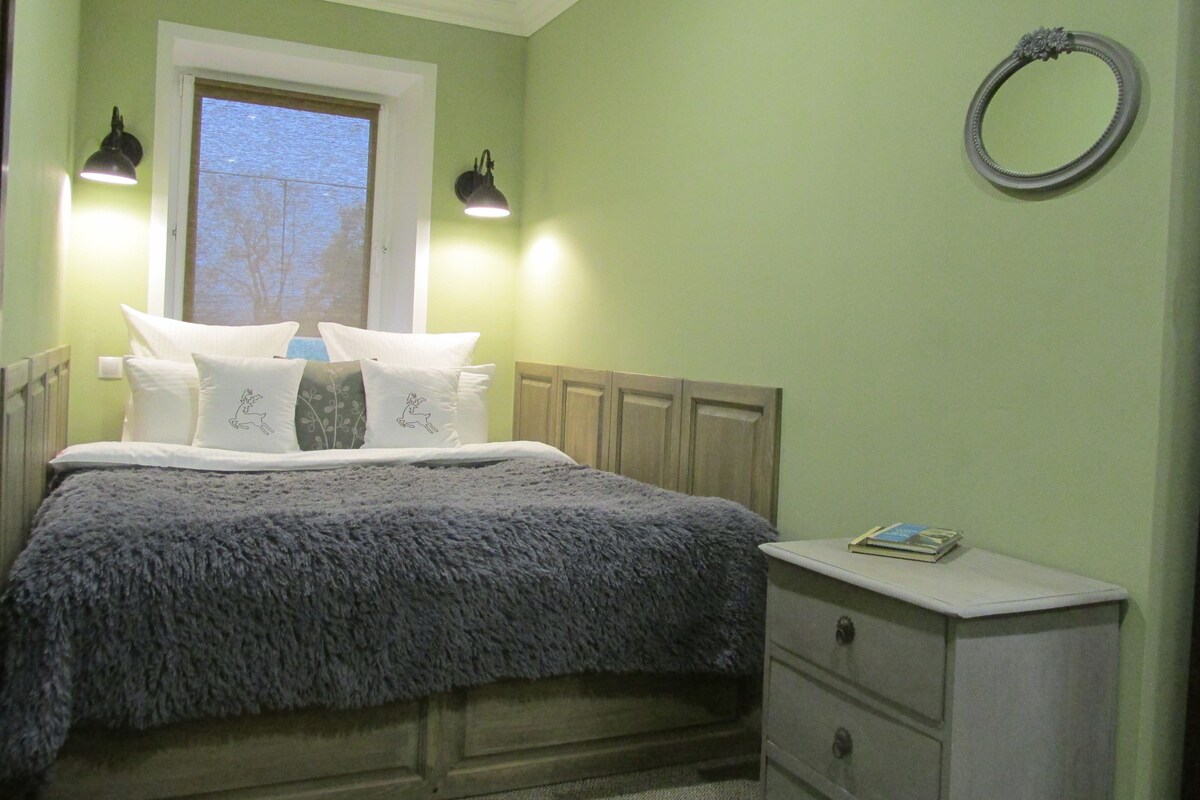 Un dormitorio con cama, almohadas, una mesita de noche y una ventana.