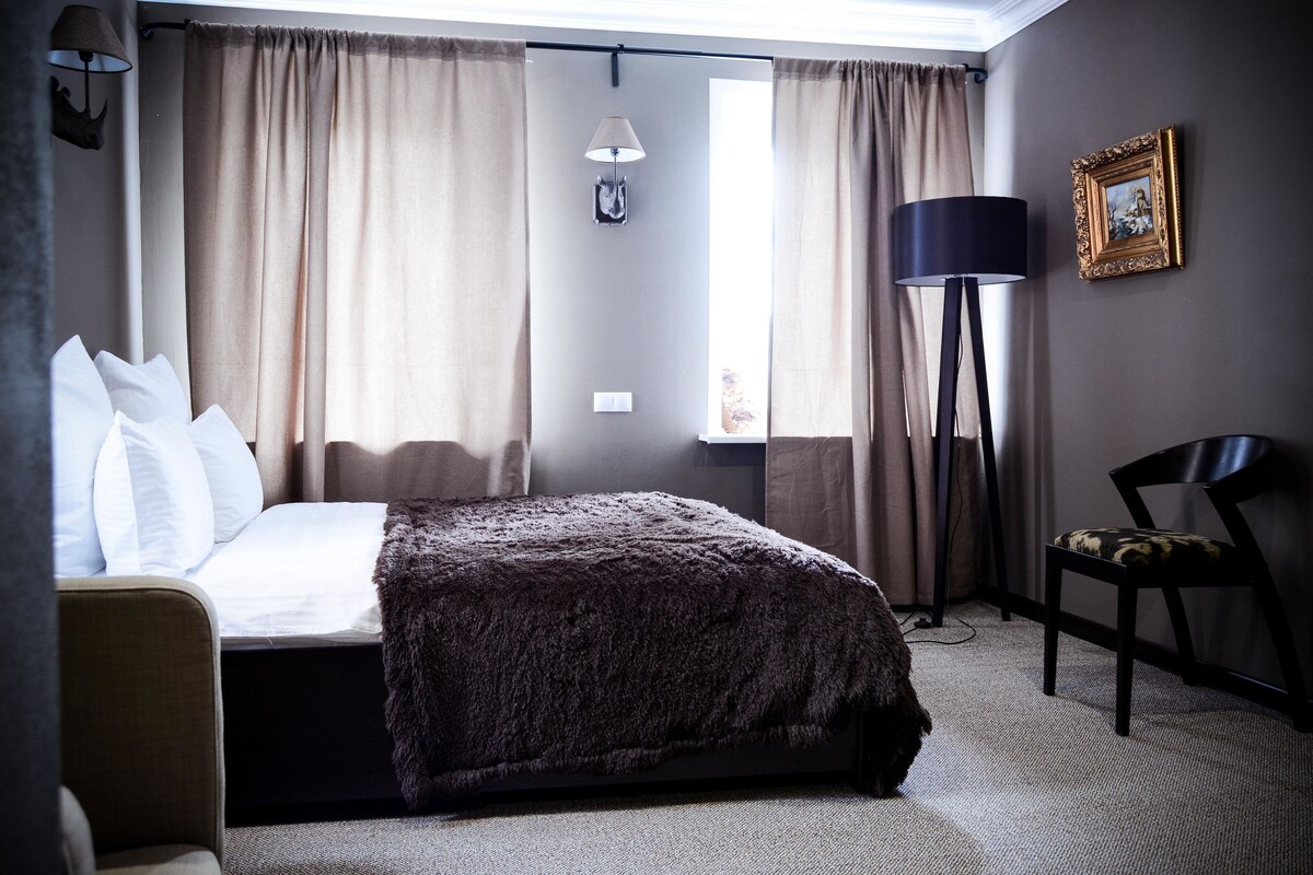 Una habitación de hotel con una cama, una silla, una lámpara y cortinas.