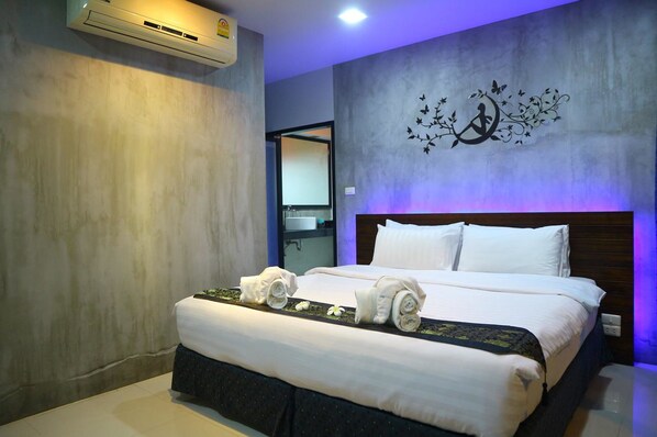 Une chambre d’hôtel moderne dotée d’un grand lit, d’une tête de lit avec éclairage d’ambiance, d’un climatiseur mural et d’une œuvre d’art décorative accrochée au mur.
