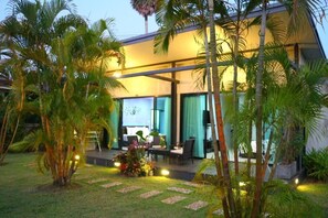 Un bâtiment moderne doté d’un espace extérieur aménagé, abrité et agrémenté de palmiers et de parterres de fleurs bien entretenus.