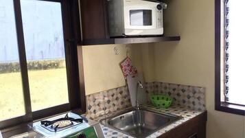 Cocina compacta con estufa a gas, microondas, pileta y ventana con vista a una zona arenosa.