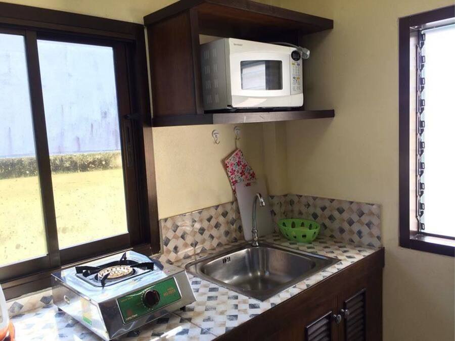 Cocina compacta con estufa a gas, microondas, pileta y ventana con vista a una zona arenosa.
