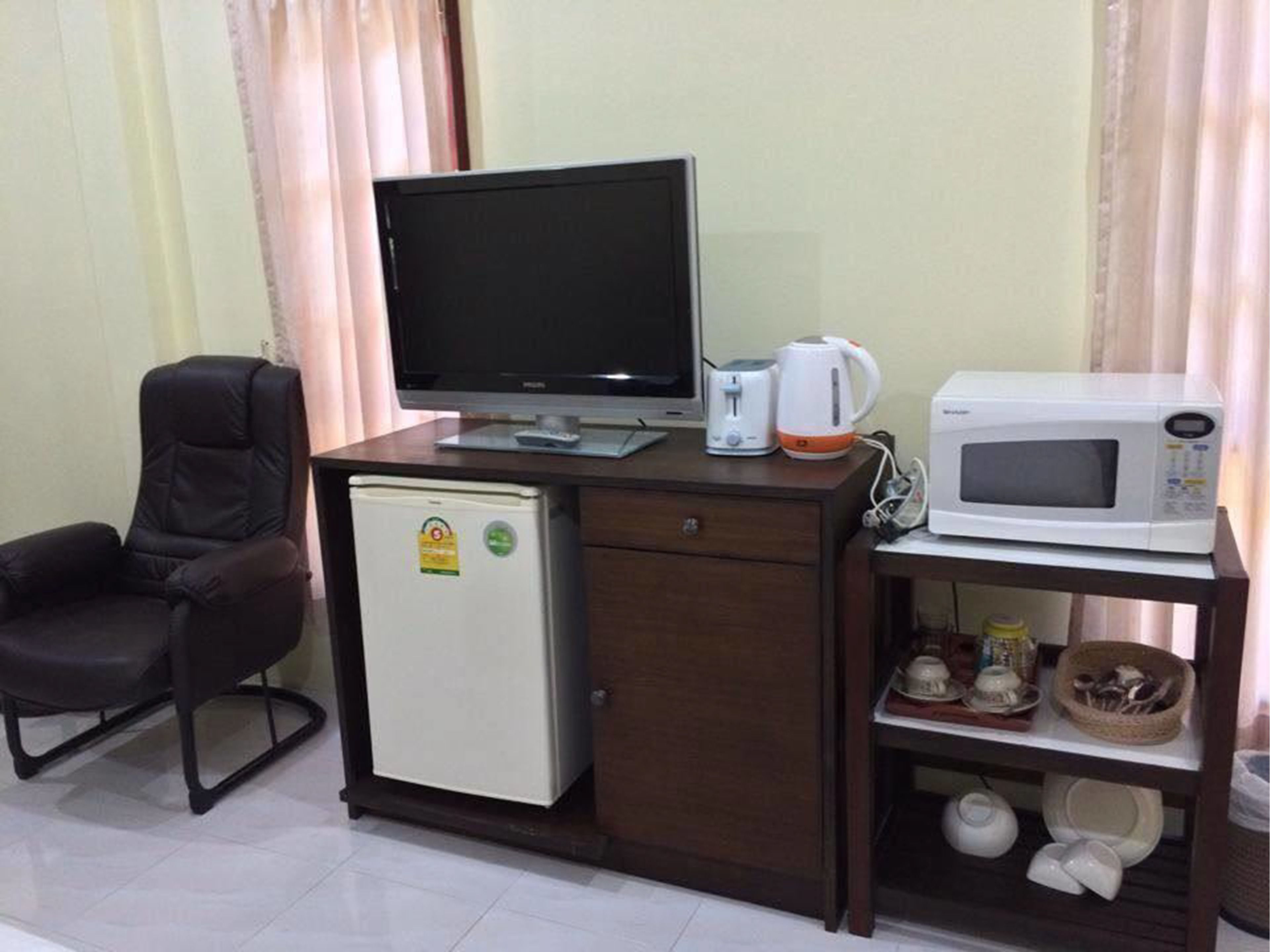 Habitación de hotel pequeña con escritorio, computadora, refrigerador compacto, microondas y una silla.