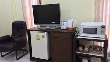 Habitación de hotel pequeña con escritorio, computadora, refrigerador compacto, microondas y una silla.