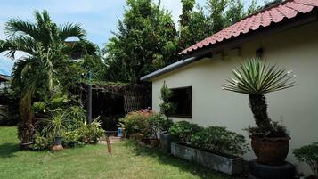 A small house with a red roof, surrounded by lush greenery and various potted plants.