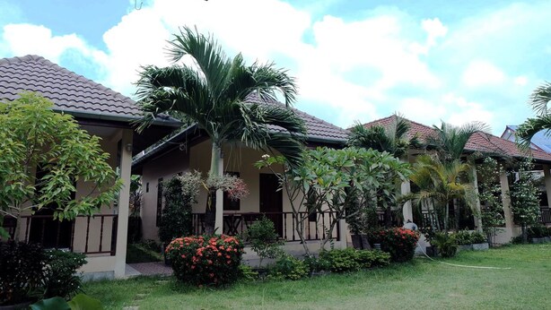 A row of houses with tiled roofs, surrounded by lush greenery and flowering plants. - Ron's Bungalow (Choeng Thale)