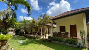 A courtyard with a lawn, palm trees, and a building with a tiled roof. - Ron's Bungalow (Choeng Thale)