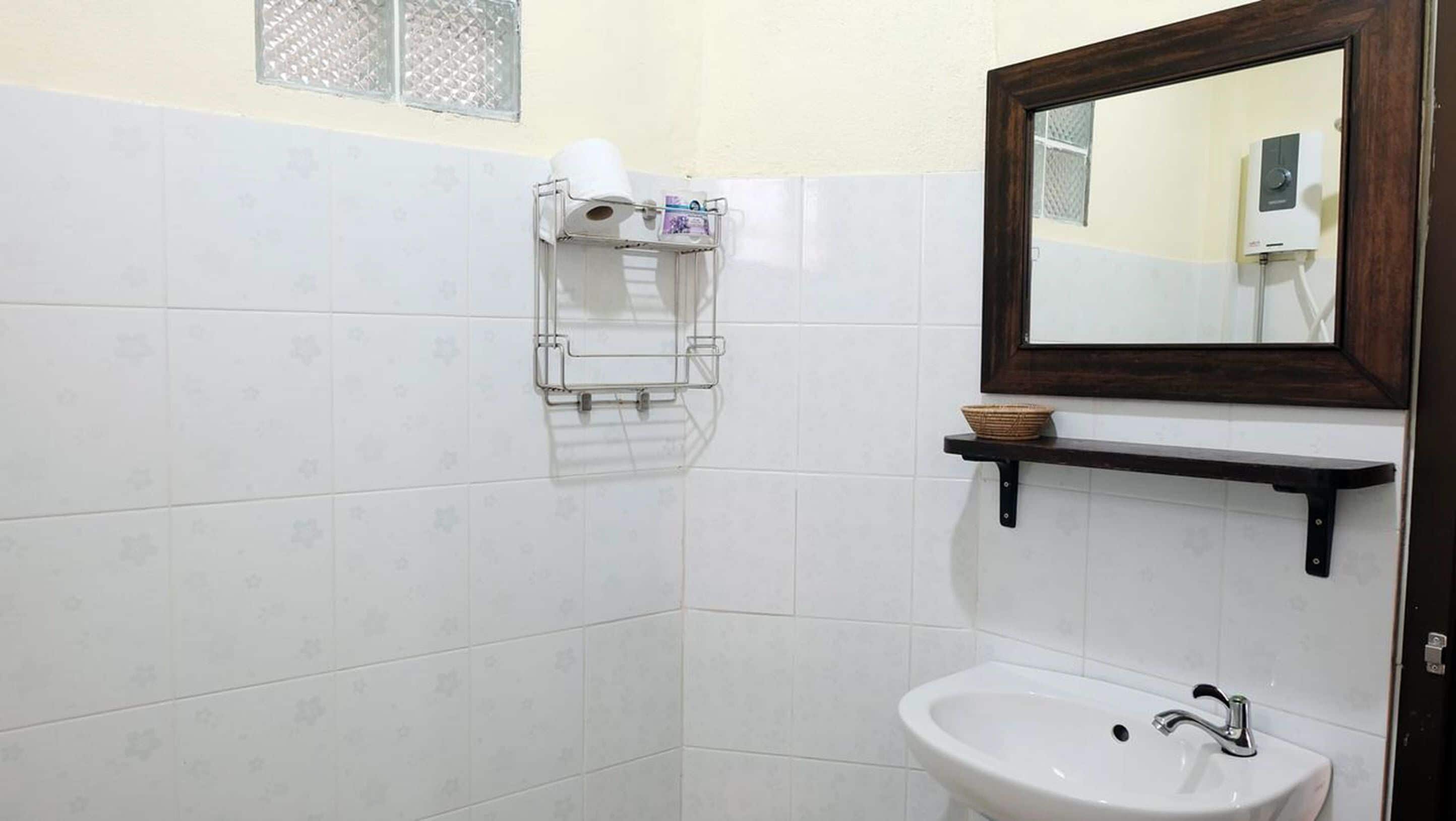 Un baño con paredes de azulejos blancos, un lavabo blanco, un espejo y un perchero para toallas.