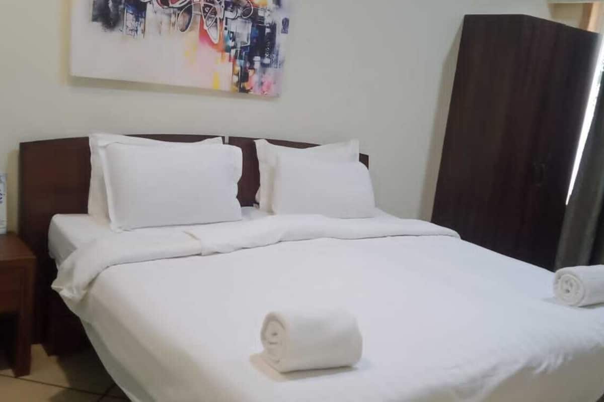 A neatly made bed with white linens and pillows, a bedside table with a phone and a small item, and a painting on the wall.