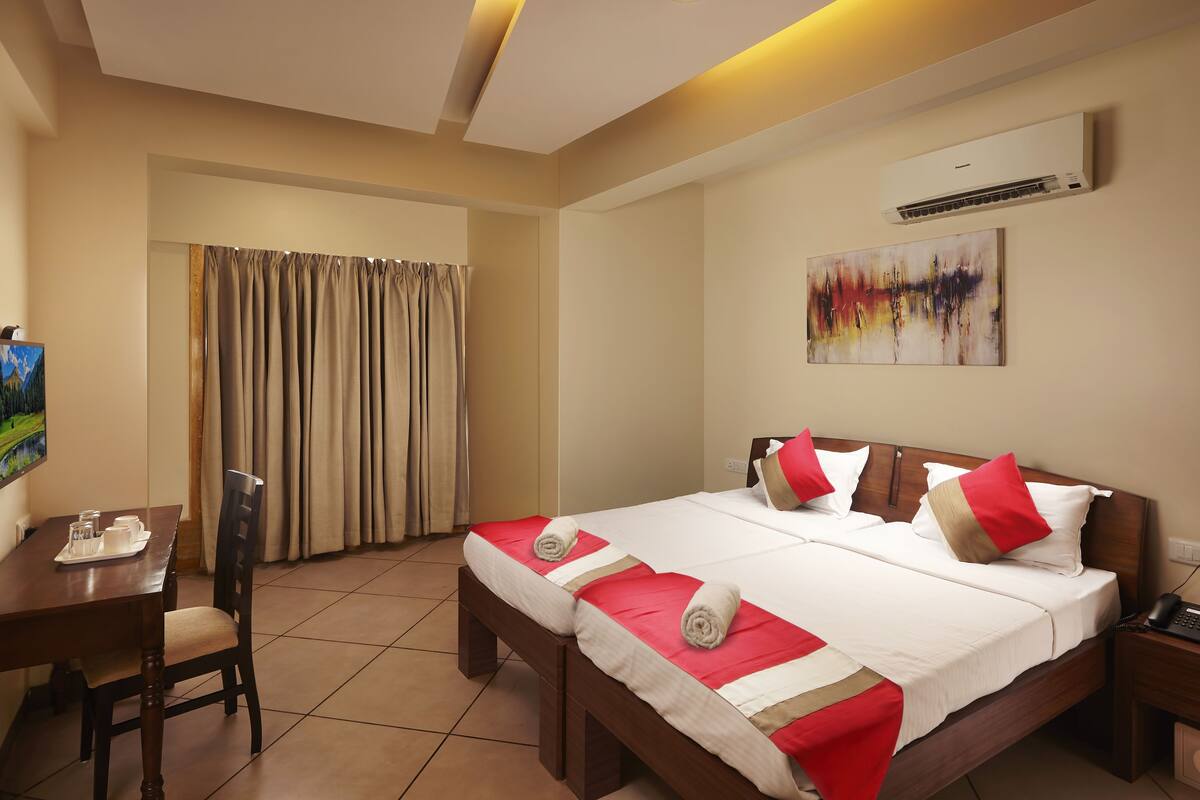 A hotel room with a bed, a desk, a chair, a TV, and an air conditioner.