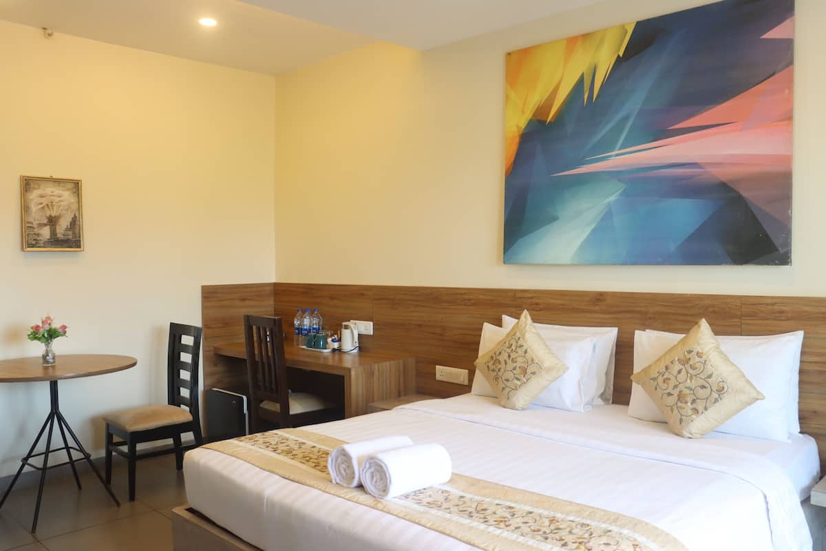 A hotel room with a bed, a desk, a chair, and a table with a vase of flowers.