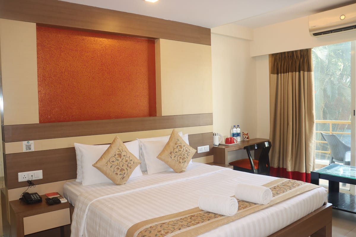 A hotel room with a large bed, a desk with a chair, a window with curtains, and a view of palm trees.