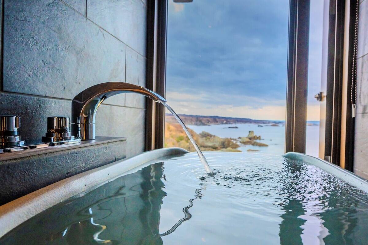 A hot tub with a view of a body of water and land, a faucet, and a control panel with knobs.