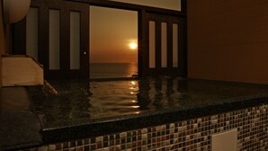 Un jacuzzi avec vue sur le coucher de soleil sur l’océan, des portes en bois et un sol carrelé.